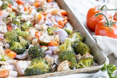 cooked vegetables like broccoli and tomato on a sheet pan with chicken