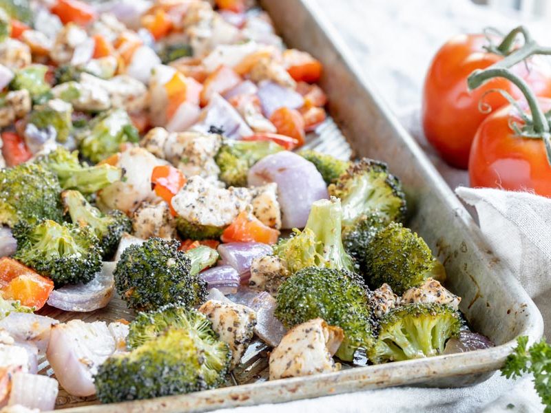 cooked vegetables like broccoli and tomato on a sheet pan with chicken