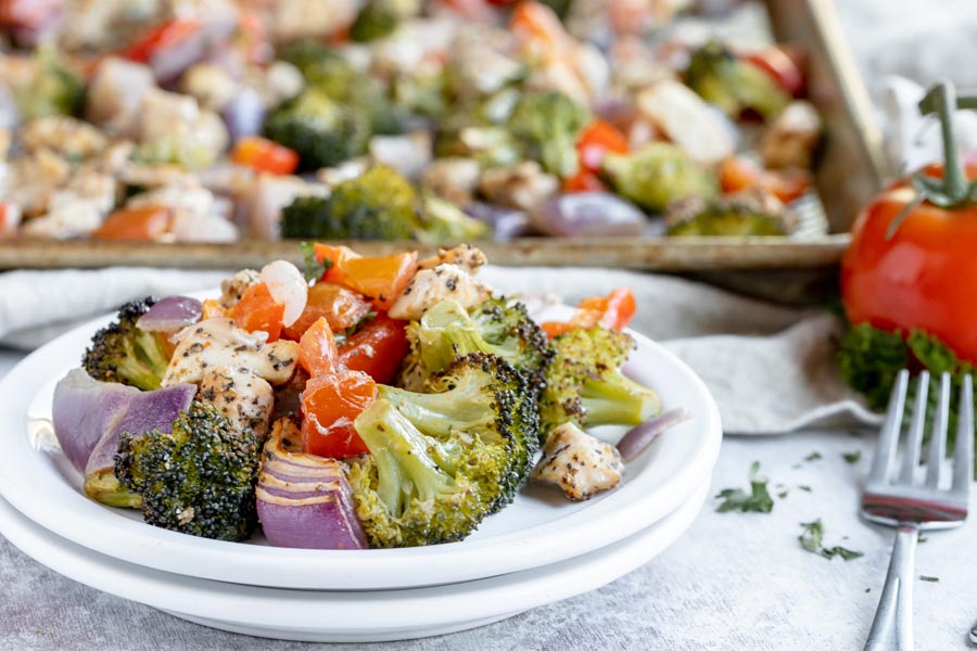 a plate with chicken and veggies on it next to a fork and a roasting pan in the background