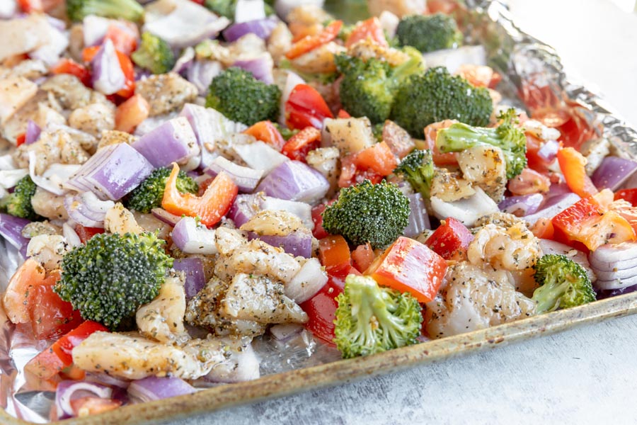 a sheet pan with raw chicken and uncooked vegetables mixed around