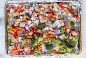 raw chicken pieces and uncooked broccoli, onion and bell pepper on a sheet pan
