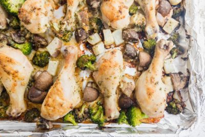 juicy chicken on a cookie sheet with roasted vegetables like mushroom broccoli and turnips