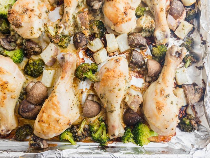 juicy chicken on a cookie sheet with roasted vegetables like mushroom broccoli and turnips