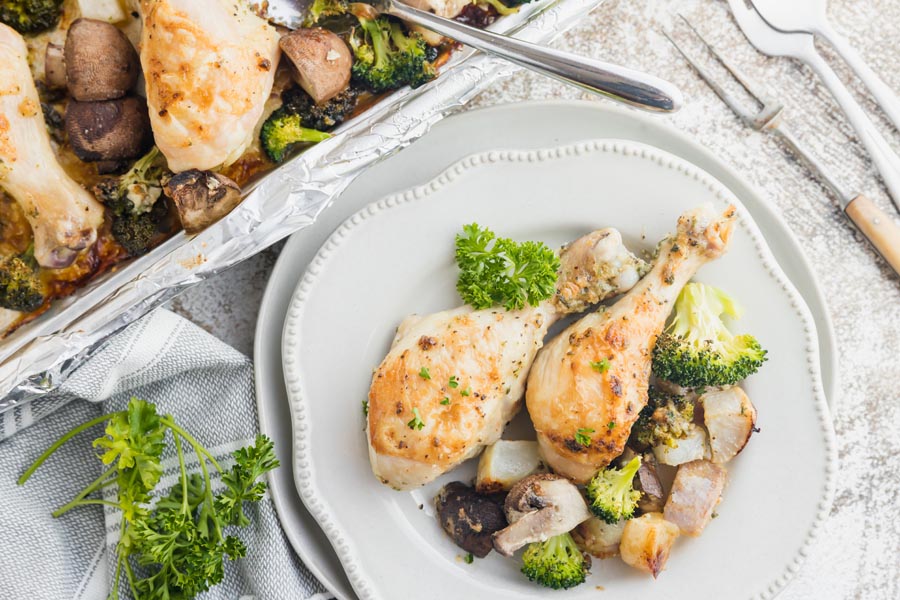 a sheet pan dinner with chicken and roasted vegetables next to a dinner plate piled with food