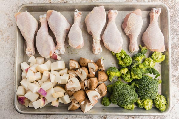 chicken legs on a baking sheet with groups of turnips, mushrooms and broccoli on it