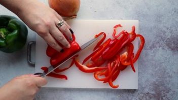 slicing a red bell pepper into thin strips