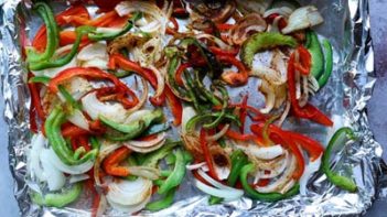 cooked sliced peppers and onions on a foil lined sheet pan