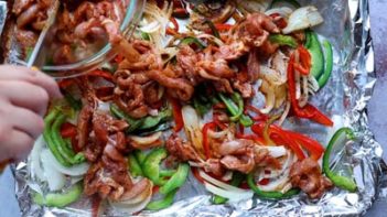 placing raw chicken strips on top of peppers and onions