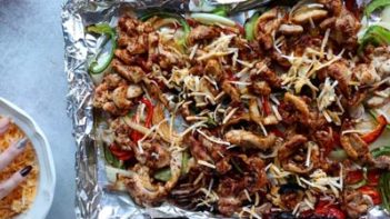 shredded cheese sprinkled on chicken fajitas in a sheet pan