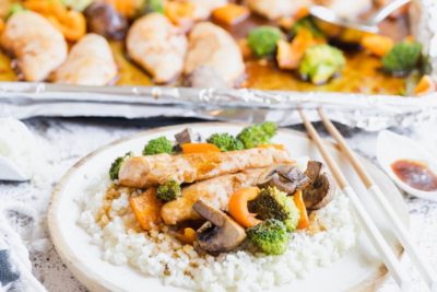 a plate of asian inspired teriyaki chicken and vegetables over cauli rice with chopsticks and a sheet pan behind