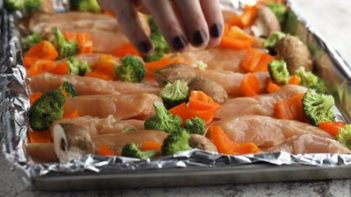 placing chicken and vegetables on a sheet pan covered in foil