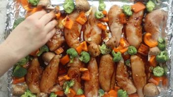 arranging bell pepper and broccoli on a baking sheet with marinated chicken