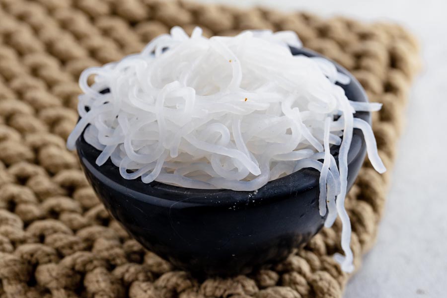 a black bowl filled with konjac noodles on a burlap pad