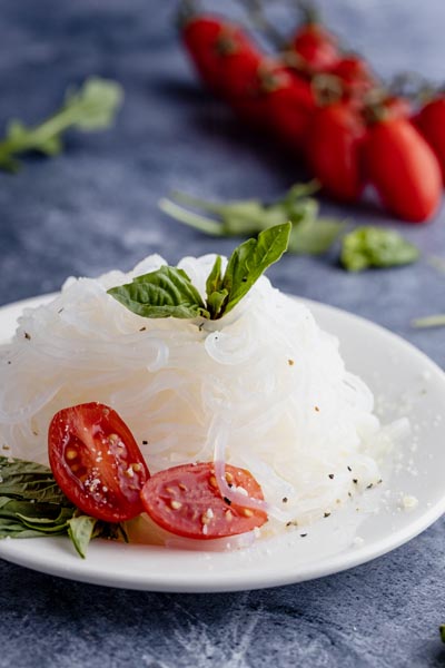 a plate of pasta with sliced tomatoes, basil and cracked pepper on top