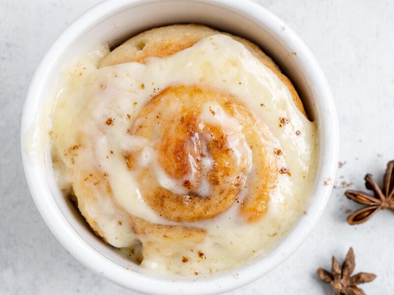 Looking down into a ramekin with a baked cinnamon roll topped with frosting inside.