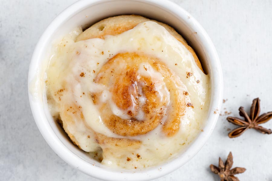 Looking down into a ramekin with a baked cinnamon roll topped with frosting inside.