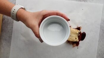 A hand holding a white ramekin over a parchment paper.