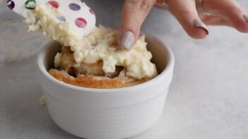 Cream cheese frosting spreading top to a single cinnamon roll with a spatula.