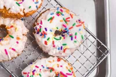 Glazed donuts covered in sprinkles on a wire rack.