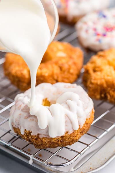 Pouring a white thick vanilla glaze on top of donuts.