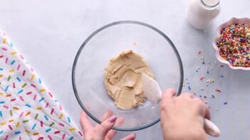 A hand mixing a pasty dough with a spatula.