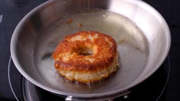A donut frying in a skillet with oil.
