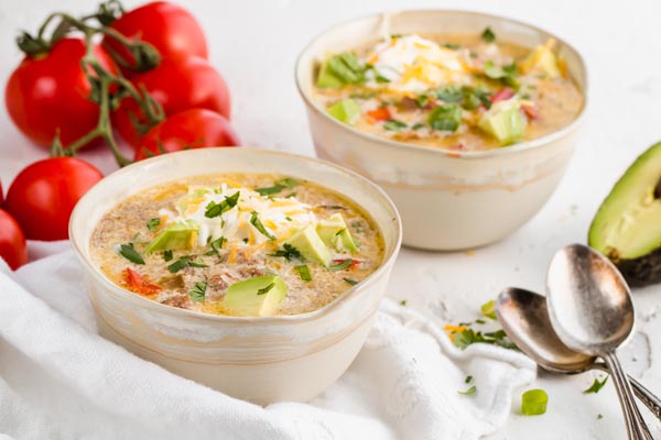 two bowls of keto taco soup topped with avocado and sour cream