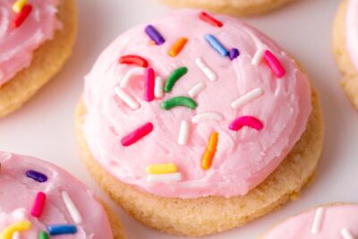 Close up of a pink frosted sugar cookie topped with sprinkles.
