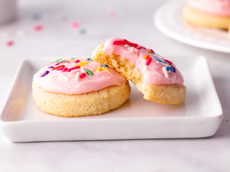 Two small sugar cookies on a white plate. One cookie has a bite taken out of it.