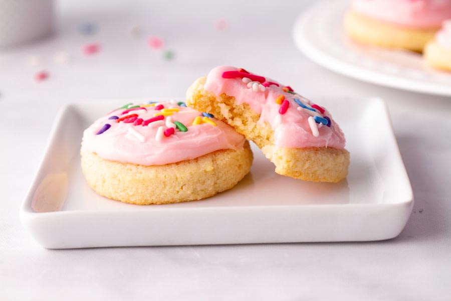 Two small sugar cookies on a white plate. One cookie has a bite taken out of it.
