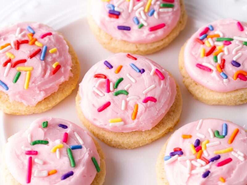 A plate of frosted pink sugar cookies with confetti sprinkles on top.