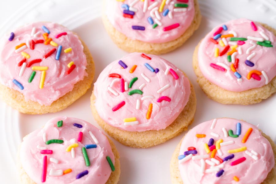 A plate of frosted pink sugar cookies with confetti sprinkles on top.