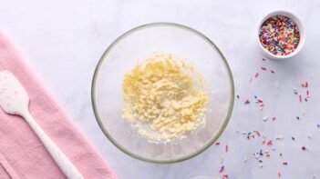 Creamed butter and sweetener in a glass bowl next to a bowl of sprinkles.