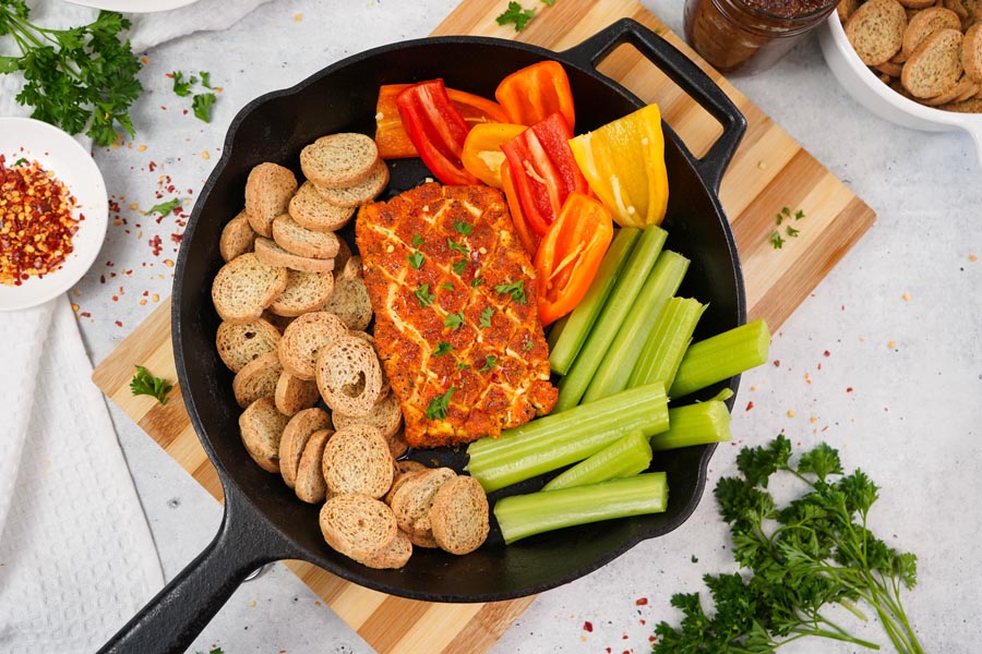 Top down view of a smoked cream cheese appetizer with celery, mini bell peppers and melba toasts surrounding the cream cheese in a skillet.