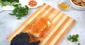 BBQ seasoning covering cream cheese on a wooden cutting board.