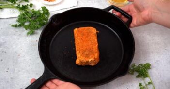 Hands holding a cast iron skillet with a seasoned block of cream cheese inside.