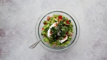 Chicken, celery, red bell pepper, cilantro, dressing and spices in a glass mixing bowl.
