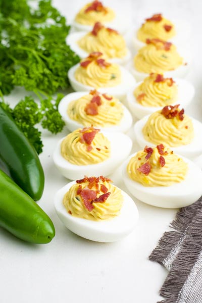 Deviled eggs on a white platter with jalapenos and parsley nearby.