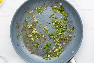 Diced jalapeno and garlic cooking in a skillet.