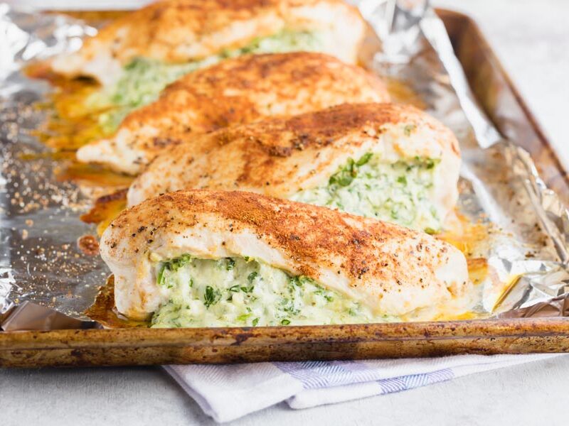a baking tray with four big pieces of chicken breast filled with a green and cheese spinach mixture