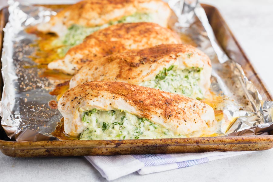 a baking tray with four big pieces of chicken breast filled with a green and cheese spinach mixture