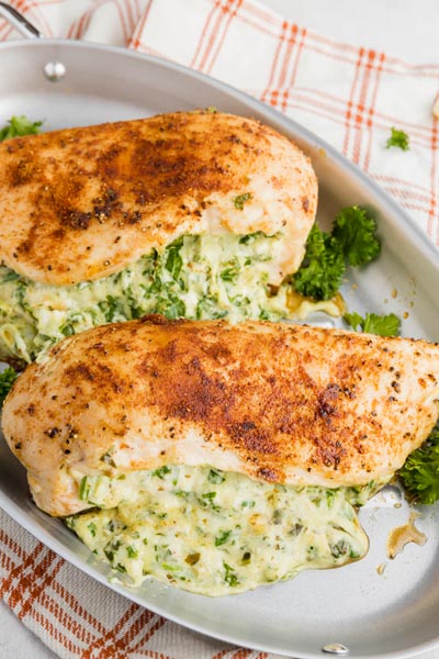two baked chicken breasts on a skillet filled with spinach and melted cheese