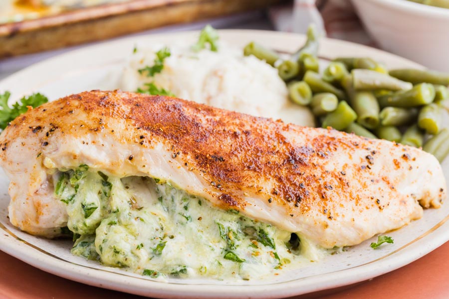 spinach and cheese filling spilling out of a piece of chicken with green beans in the background