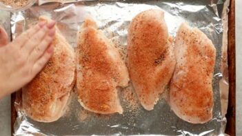 patting seasoning on top of four chicken breasts