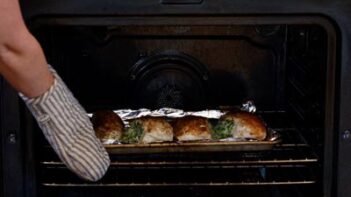 pulling a baking tray out of the oven with stuffed chicken breast on it