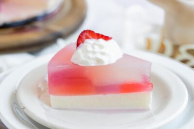 A wedge of layered stained glass cake topped with whipped cream and a strawberry slice.