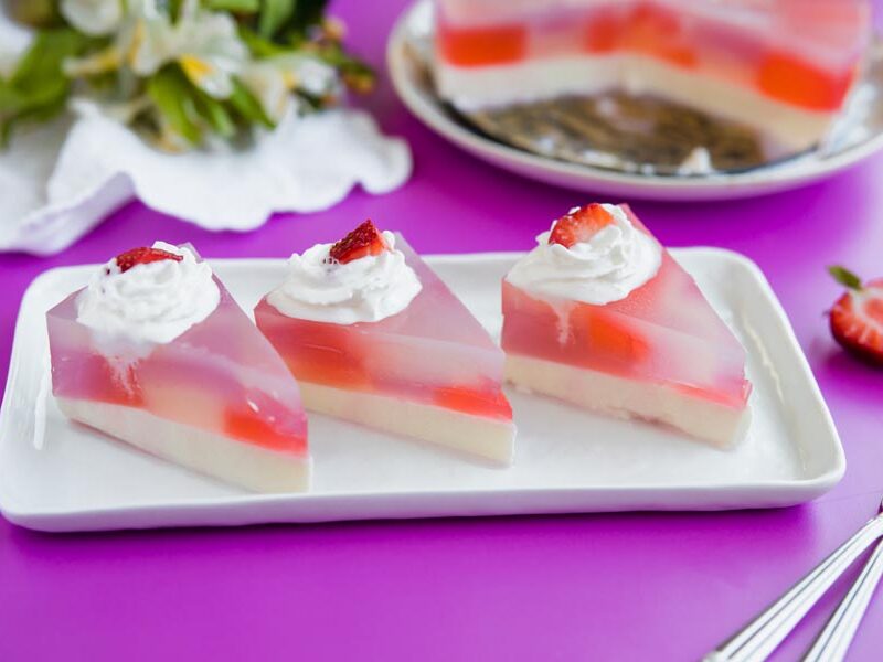Three slices of stained glass cake topped with whipped cream and strawberries.