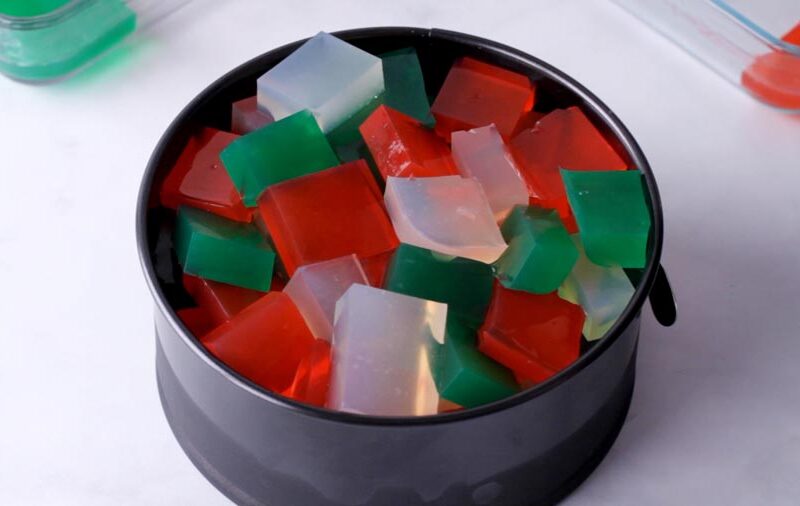 Black springform pan filled with red, green, and translucent gelatin cubes.