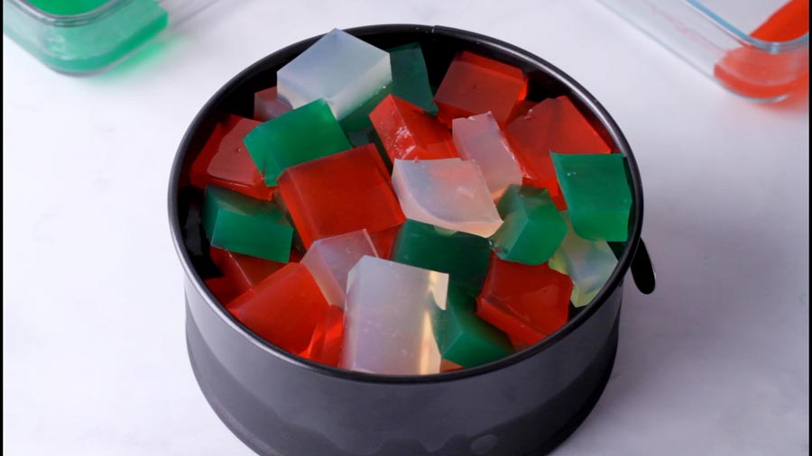 Black springform pan filled with red, green, and translucent gelatin cubes.