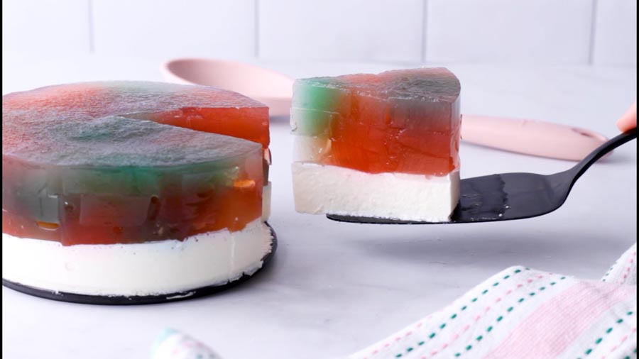 A slice of stained glass cake being lifted from a full cake, showing colorful layers.